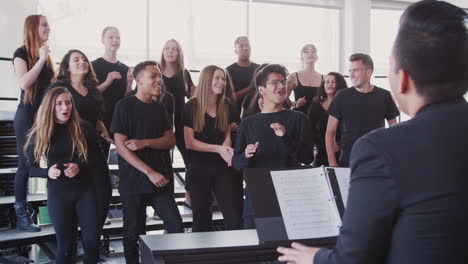 male and female students singing in choir with teacher at performing arts school