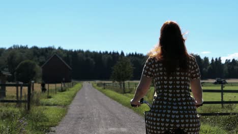 Frau-Mit-Kleid-Fährt-Fahrrad-Auf-Der-Landstraße