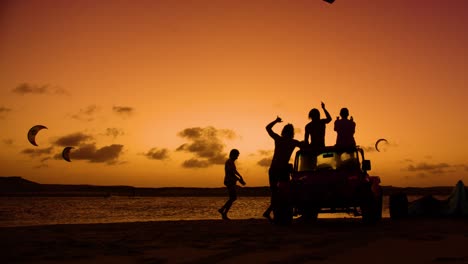 Kiteboarder-jumps-in-front-of-cheering-friends---silhouettes-against-sunset-sky