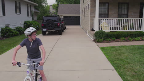 a boy on his bike wait at the end of his driveway to start his ride as camera pulls back and up