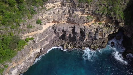 Aerial,-approaching-waves-crashing-on-a-sea-cliff