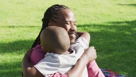 video of happy african american father and son having picnic on grass and hugging