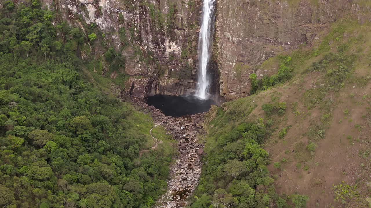 Waterfall plunging into dark pool, surrounded by cliffs and green hills in Brazil