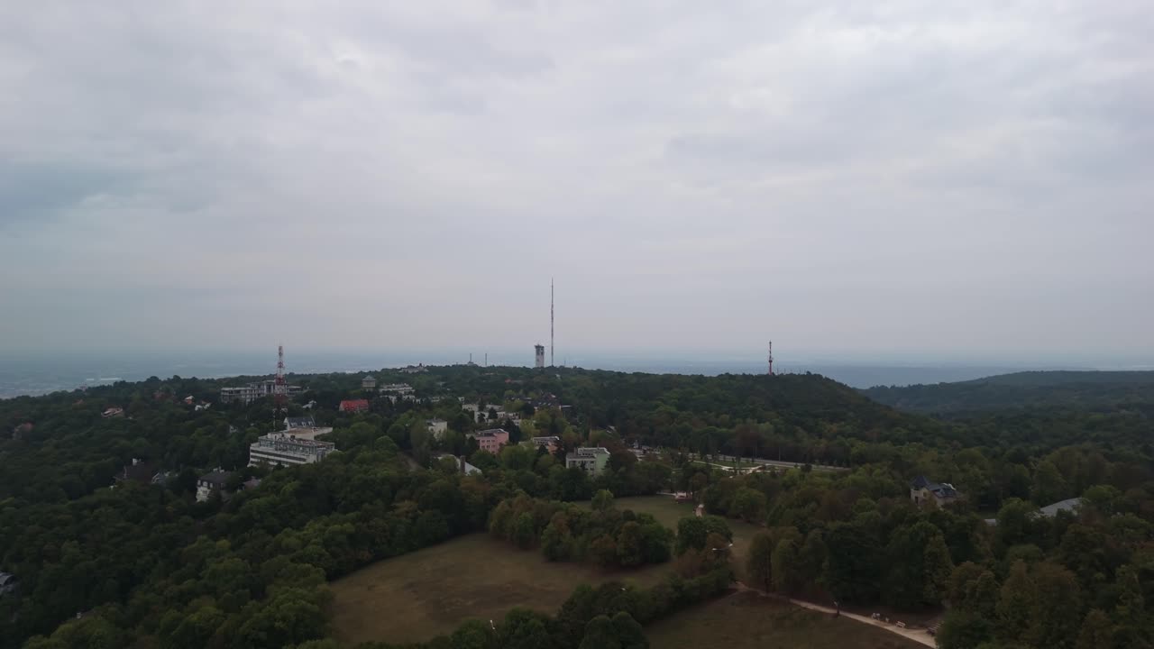 Orbital drone view from Normafa with the surrounding radio towers on the Széchenyi-hegy under a cloudy sky in Hungary