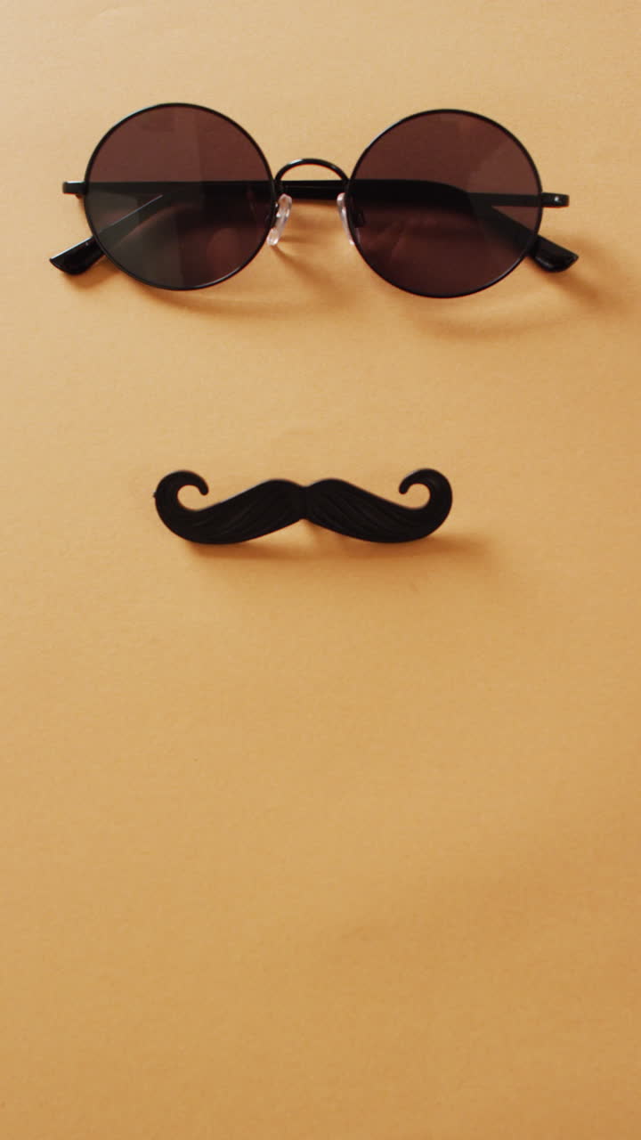 Vertical video of round sunglasses and black false moustache on orange background with copy space