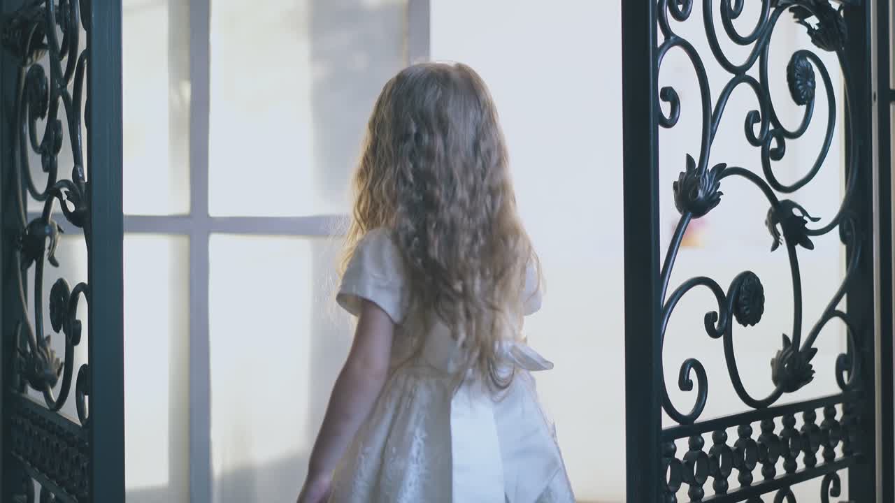 chica linda en vestido festivo abre la rejilla forjada de la puerta de la habitación