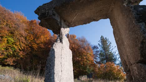 sliding shot of an abandoned concrete door frame surrounded by trees changing color in the autumn weather