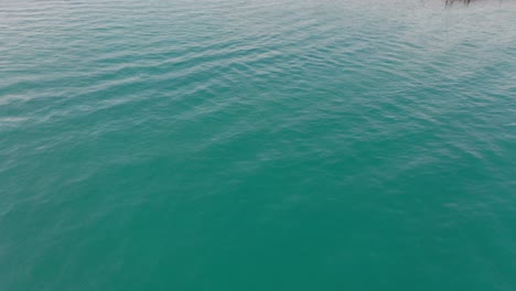 Drone-flying-over-beautiful-lake-Geneva-and-revealing-a-small-yacht-leaving-harbor-in-Lausanne,-Switzerland