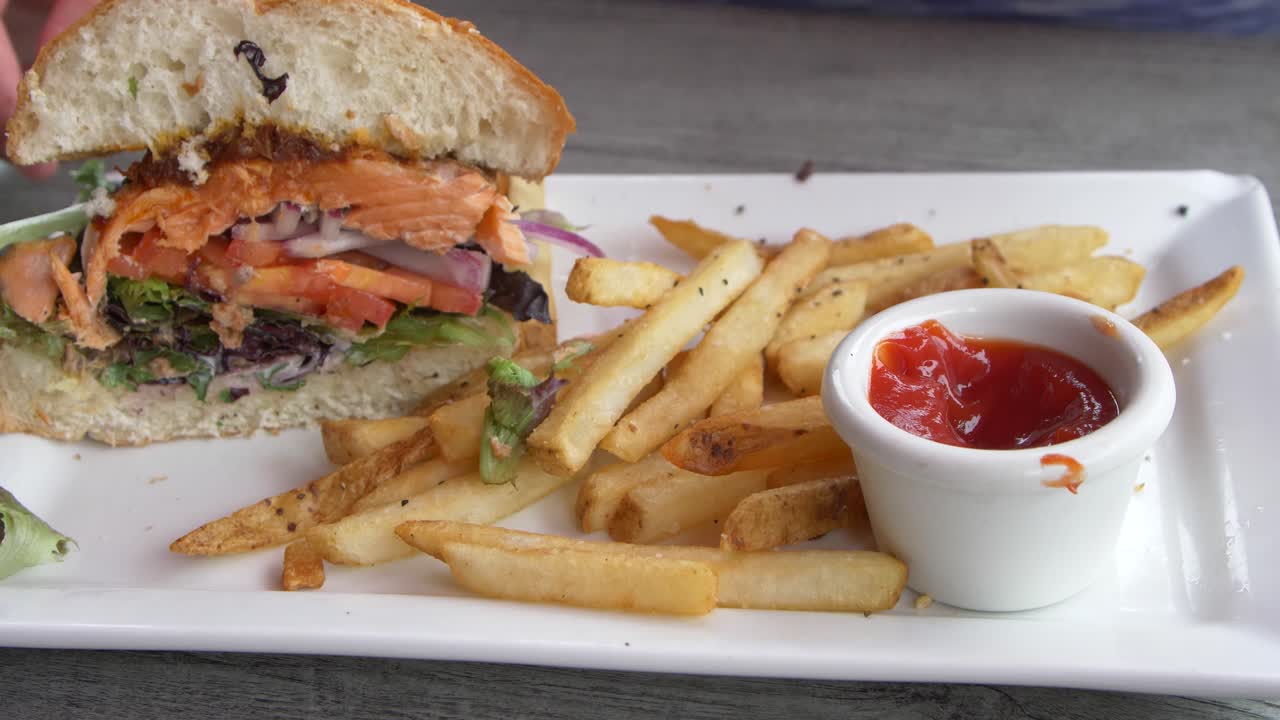 연어 버거를 먹고 감자튀김을 케첩에 찍어먹는 사람