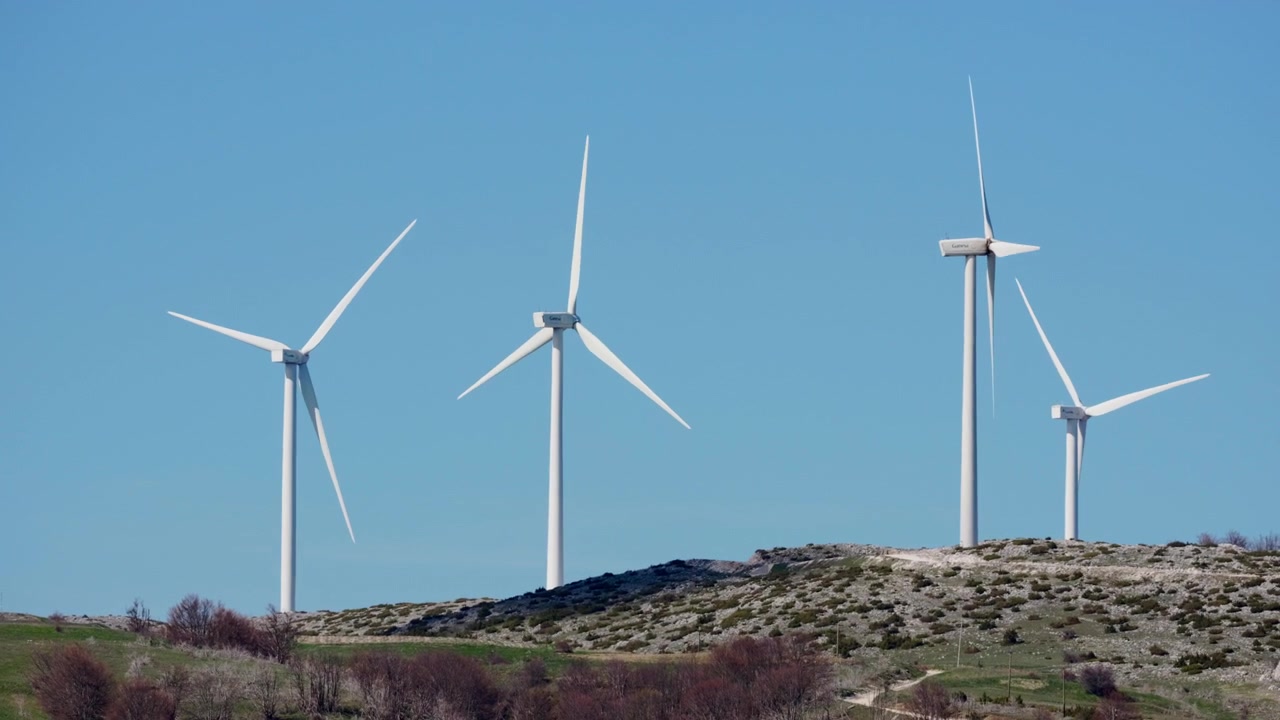 Due turbine eoliche si ergono su un paesaggio roccioso, le loro pale girano dolcemente sotto un cielo azzurro brillante. Ideale per contenuti sull'ambiente o sull'energia rinnovabile