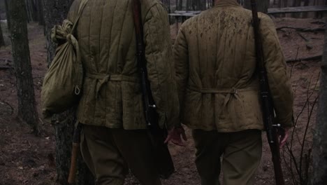 dos soldados de la segunda guerra mundial caminando en un bosque con rifles, cascos y botas