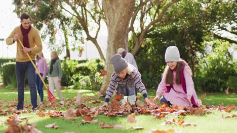 video of happy caucasian son and daughter throwing autumn leaves while father rakes them up