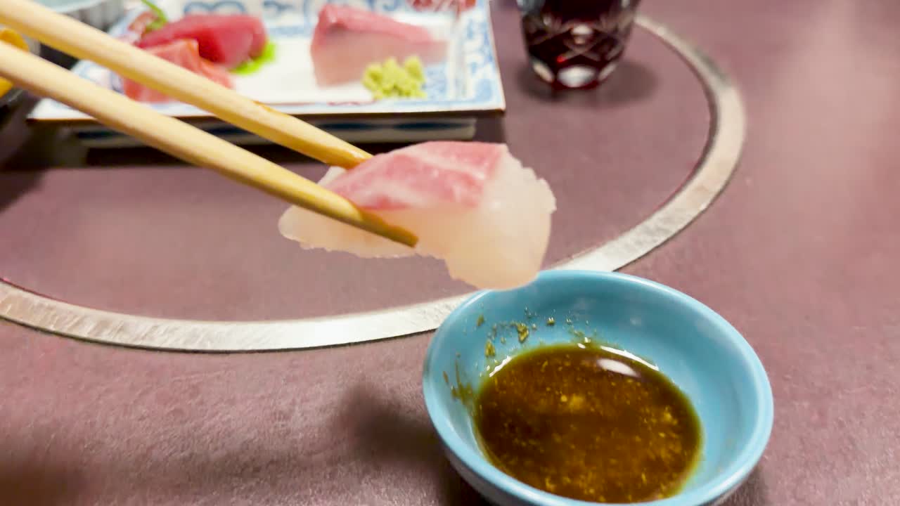 Primo piano di bacchette che prendono pesce crudo e lo intingono nella salsa di soia.