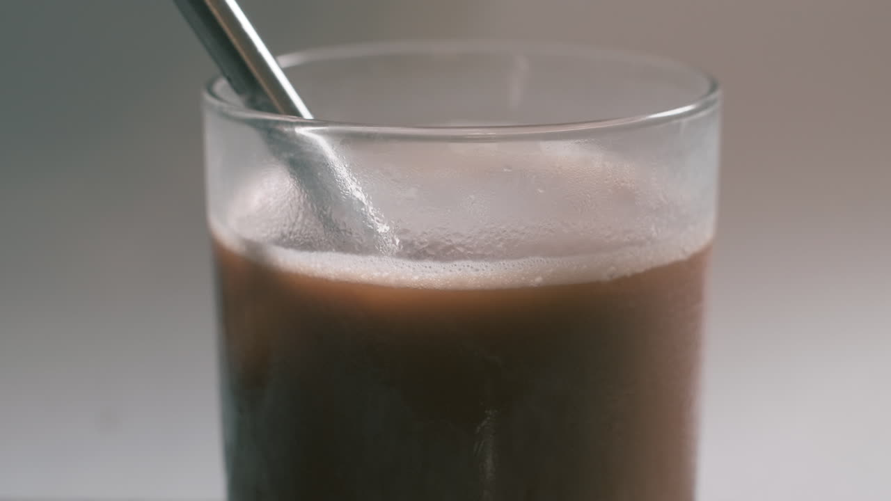 Caffè ghiacciato in un bicchiere sorbito con una cannuccia in acciaio inossidabile - primo piano.