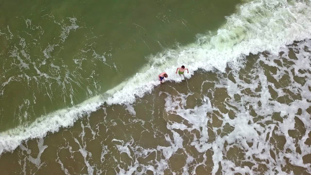 dos niños jugando en el mar con olas rompiendo en la orilla