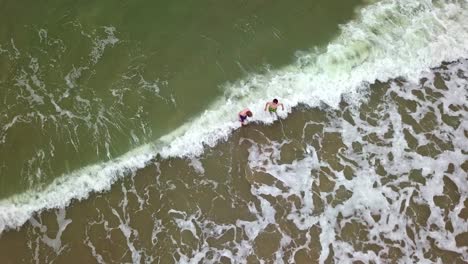 Dos-Niños-Jugando-En-El-Mar-Con-Olas-Rompiendo-En-La-Orilla