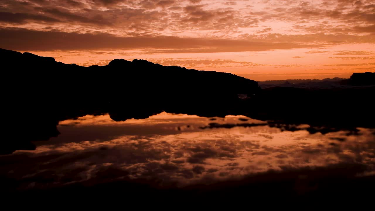 Goldene Himmelsspiegelung in Felsbecken bei Sonnenuntergang, Meereswellen rollen herein