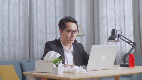 sick asian businessman holding a thermometer to the video call with doctor on a laptop while working at home