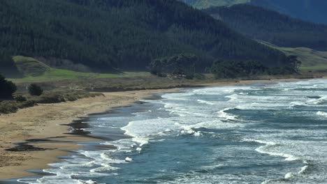 Long-rolling-waves-hitting-shore-of-Ocean-Beach-in-New-Zealand,-aerial