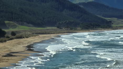 long rolling waves hitting shore of ocean beach in new zealand, aerial