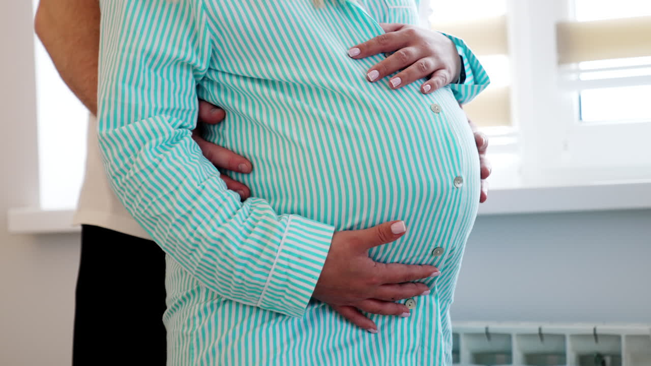 Unrecognized pregnant lady stroking big belly. Male hands touching the abdomen. Close up.