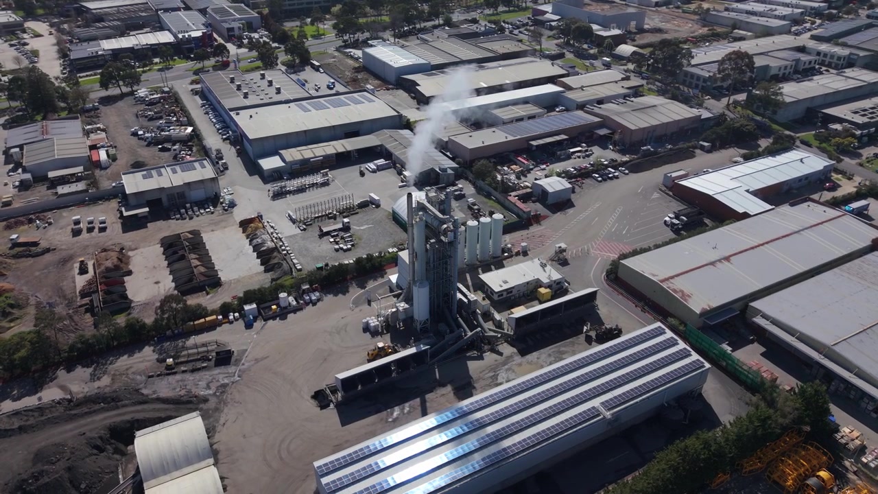 High angle aerial view of an industrial area with a smoking asphalt plant and solar panels on roofs
