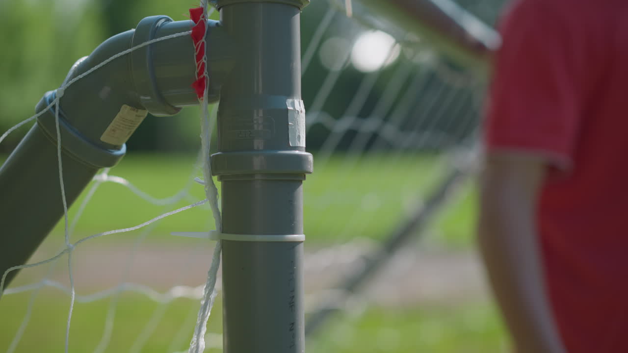Close-up of a soccer goalpost with a ball already shot into the net, showing a blurred view of the goalkeeper reaching to retrieve the ball after it has entered