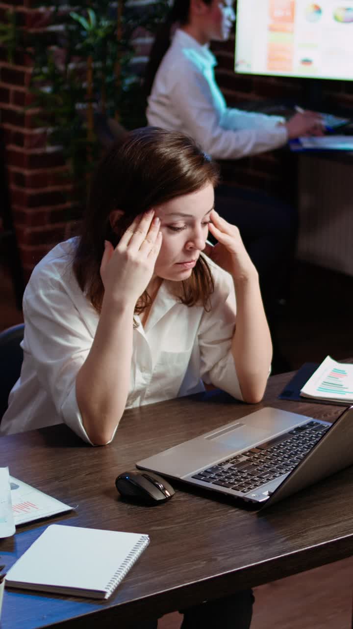 Video verticale. Dipendente stanco che lotta per rimanere concentrato alla scrivania in ufficio, sentendosi sovraccarico di lavoro