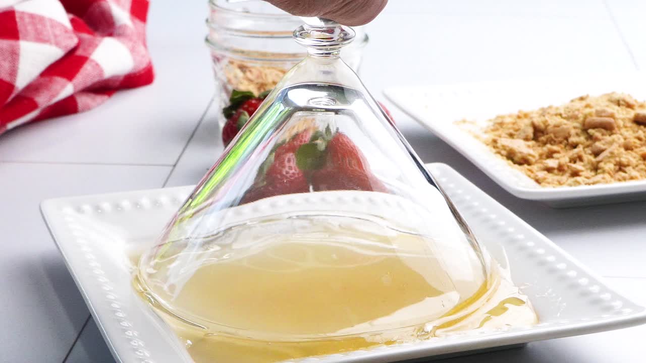 Dipping and rolling a martini cocktail glass into honey on a white plate. Making a cocktail and putting honey on the rim. Strawberry shortcake martini as a dessert drink with fresh berries.