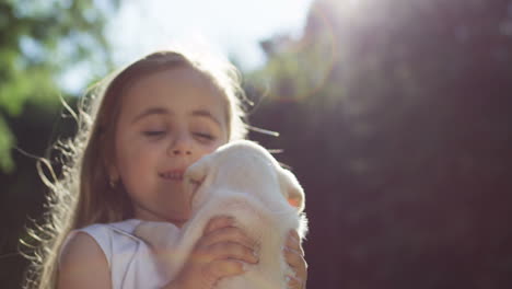 close-up view of a caucasian little girl spinning around while holding a small labrador puppy and playing with it in the park on a summer day