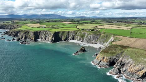 drone coast of ireland copper coast waterford emerald green seas and a patchwork of farmland under the comeragh mountain range last day of summer