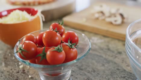 Bowls-of-tomatoes,-grated-cheese-with-sliced-mushrooms,-pizza-ingredients-in-kitchen,-in-slow-motion