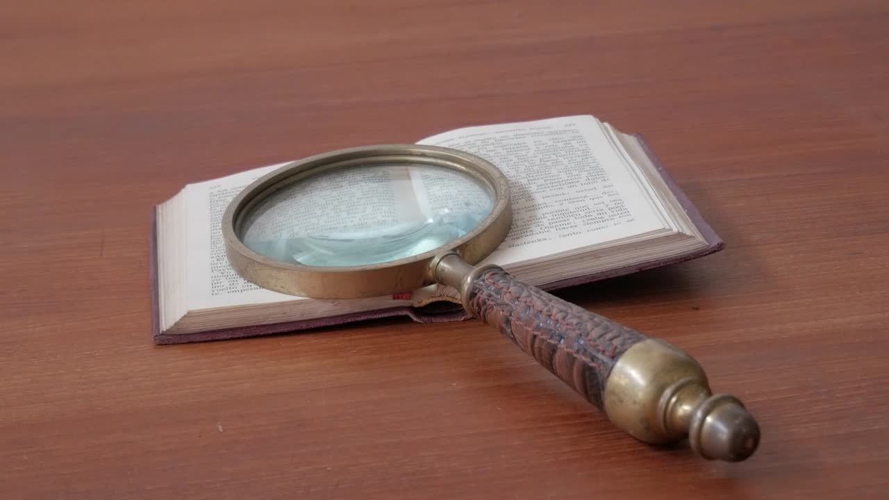 Zoom out from an antique magnifying glass placed over an open book on a wooden table