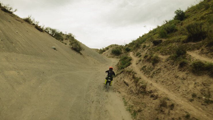 Skilled rider drives vehicle along hollow between hills fpv. Motorcyclist on offroad motorbike trains for motocross racing. Motorcycling in wilderness
