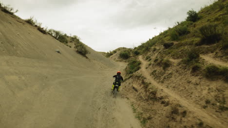 skilled rider drives vehicle along hollow between hills fpv. motorcyclist on offroad motorbike trains for motocross racing. motorcycling in wilderness