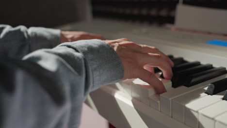 vista de cerca de una mano con una camisa de manga azul tocando con gracia las teclas del piano, con un fondo suavemente borroso. el enfoque en la mano captura el movimiento delicado y la expresión de la música