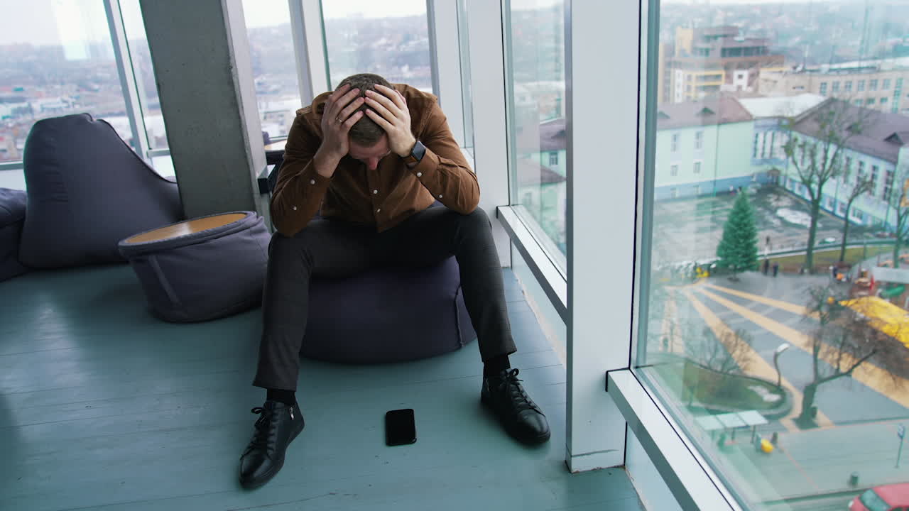 Businessman sitting in office by the large window. Thoughtful man with his hands on eyes becomes happy after finding the solution to the problem.