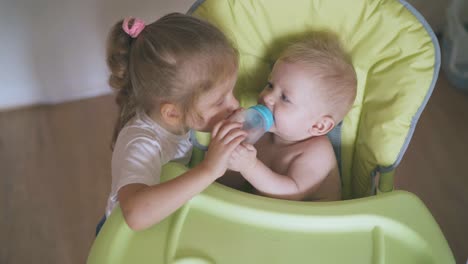 girl-gives-to-drink-water-boy-sitting-in-green-highchair