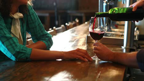 Barman-serving-red-wine-to-female-customer-at-bar-counter