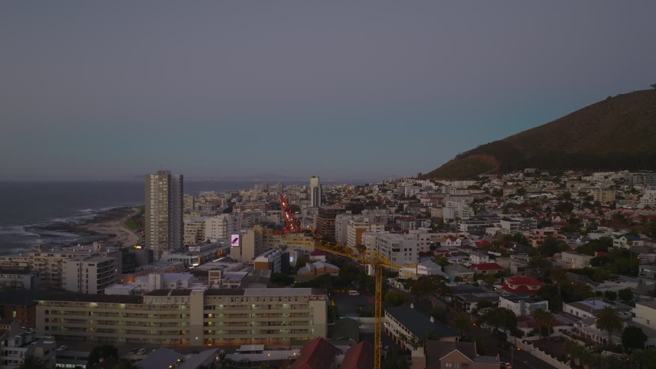 forwards vuela sobre la ciudad al crepúsculo. edificios de apartamentos de varios pisos a lo largo de la calle y el mar en el fondo. ciudad del cabo, sudáfrica