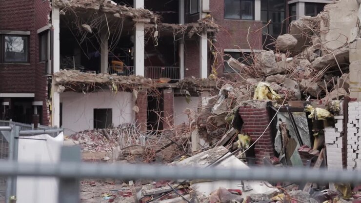 An excavator is demolishing a house from the inside out! In the foreground is a fenced off building site,