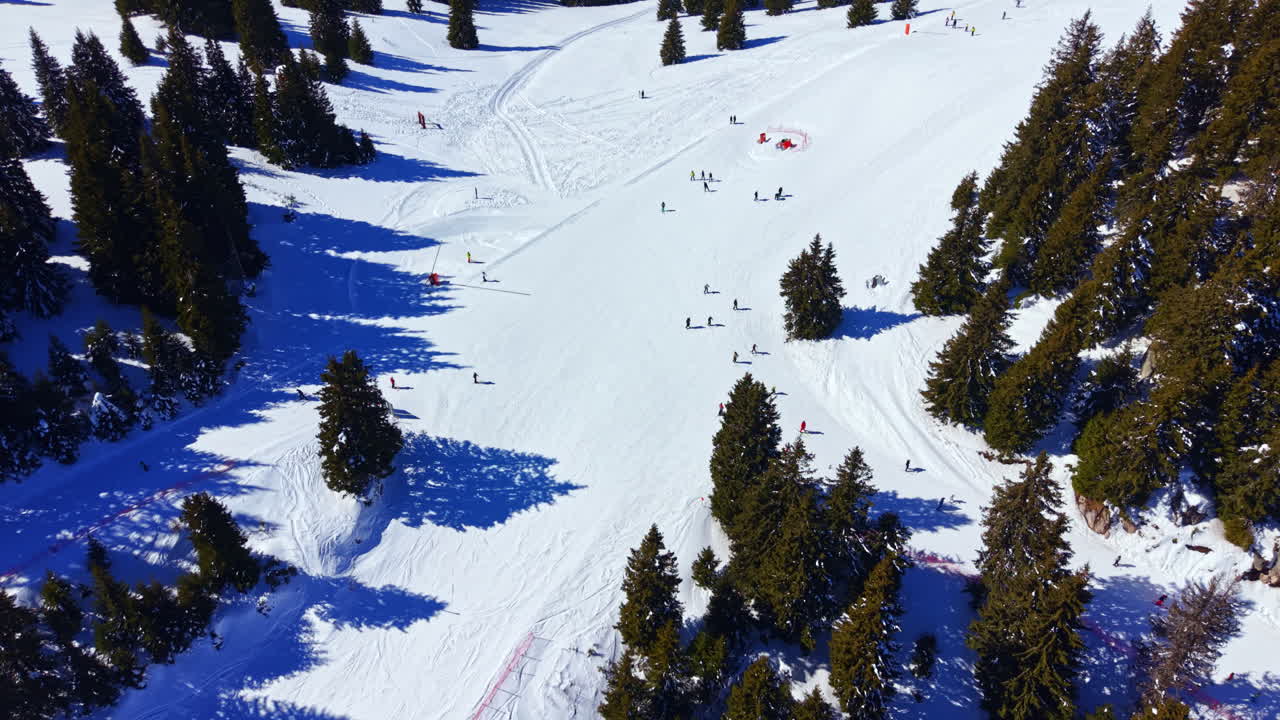 Vista aerea di una stazione sciistica con persone che sciano e fanno snowboard in una soleggiata giornata invernale.