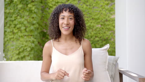 smiling woman sitting on couch outdoors, gesturing with hands while talking, on video call