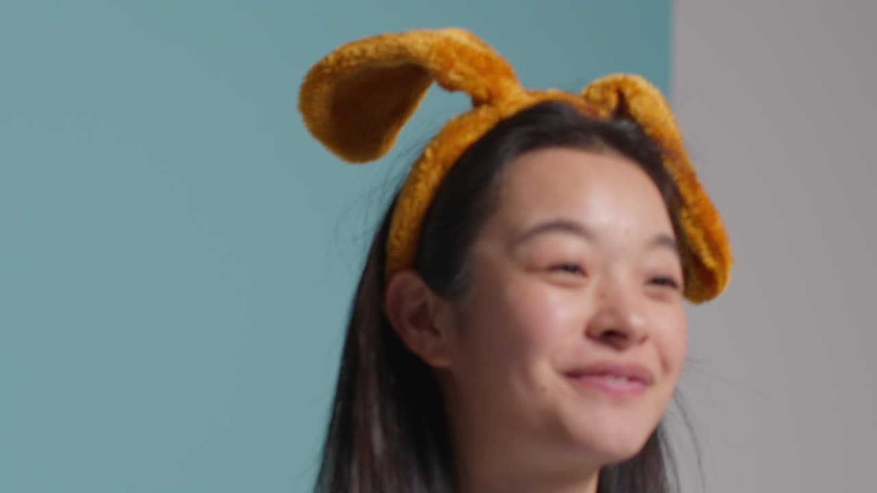 푸른 스튜디오 배경 앞에 있는 젊은 여성이 옷을 입고 사진 부스 스타일의 초상화를 위해 포즈를 취하고 있습니다.