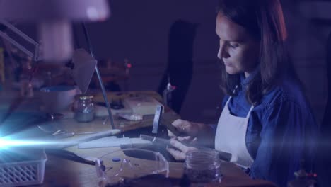 Animation-of-glowing-light-over-caucasian-woman-using-tools-working-in-workshop