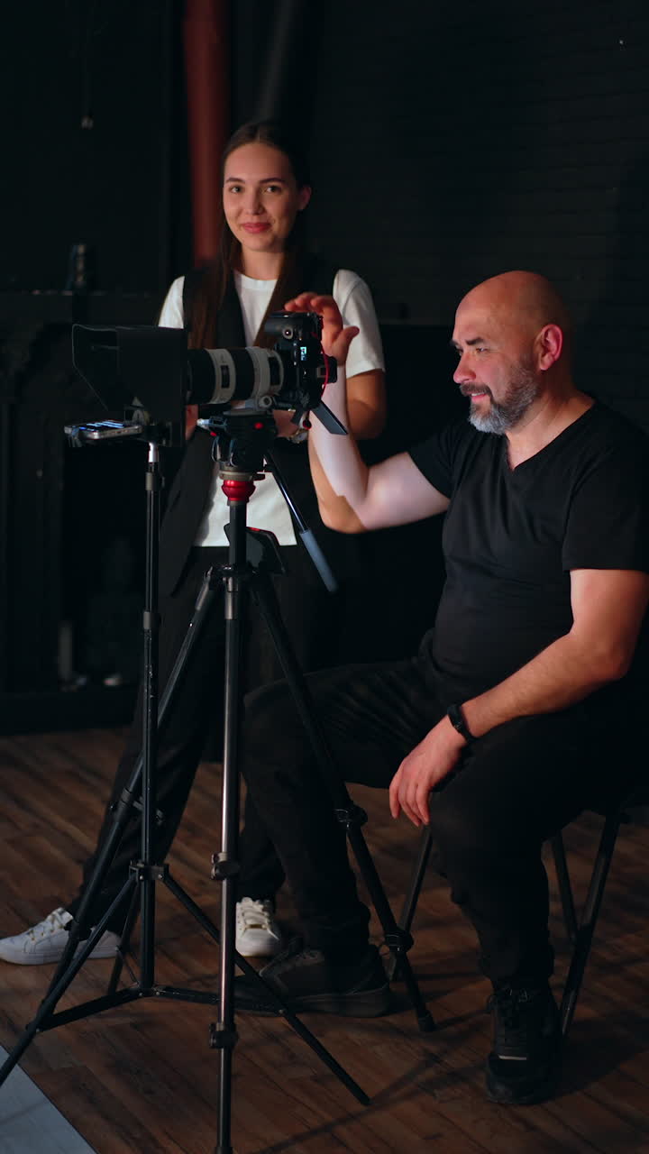 Positive man and woman working backstage in studio. People taking video using professional equipment. Vertical video