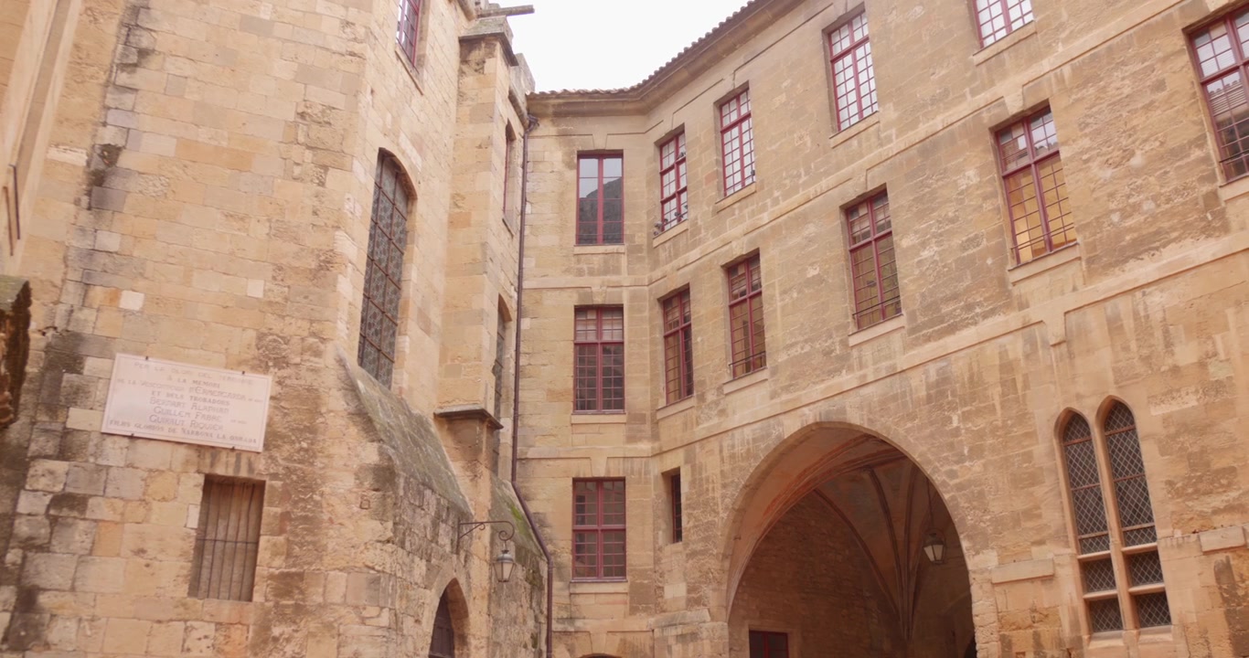 Ripresa panoramica del cortile interno del Palazzo Arcivescovile di Narbonne, medievale e neoclassico, con antiche mura in pietra e architettura ad arco, nel sud della Francia.