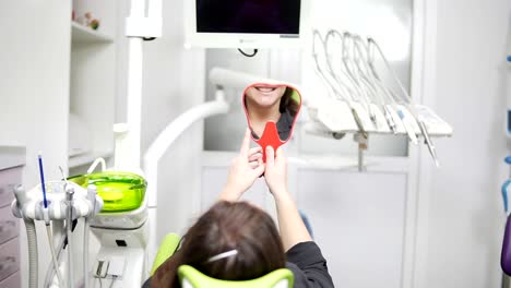 Young-beautiful-woman-in-the-dental-chair.-After-the-procedure-she-looks-in-the-mirror.-The-concept-of-a-healthy-smile