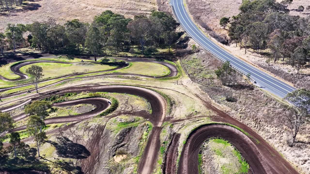 Drone captures winding motocross track, dirt paths, and surrounding dry landscape in bright daylight
