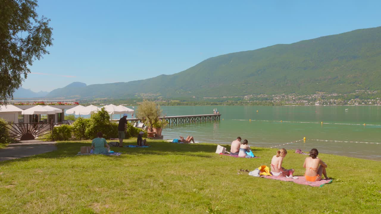 Profile view of tourists sunbathing at "Lac du Bourget" (Bourget Lake), the biggest natural lake in Aix-les-Bains, France. 4k.